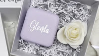 Astuccio in similpelle viola personalizzato “Glenda” con effetto lamina metallizzata tramite incisione laser, in una scatola regalo con rosa bianca.